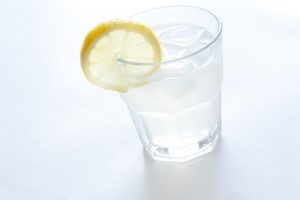 Gin and tonic on ice with lemon in a plain glass tumbler for a refreshing alcoholic beverage on a white background